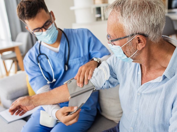 A clinician taking an older patient's blood pressure at home.