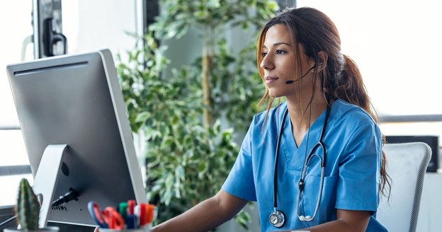 A clinician wearing a headset at a monitor, taking a remote consultation.